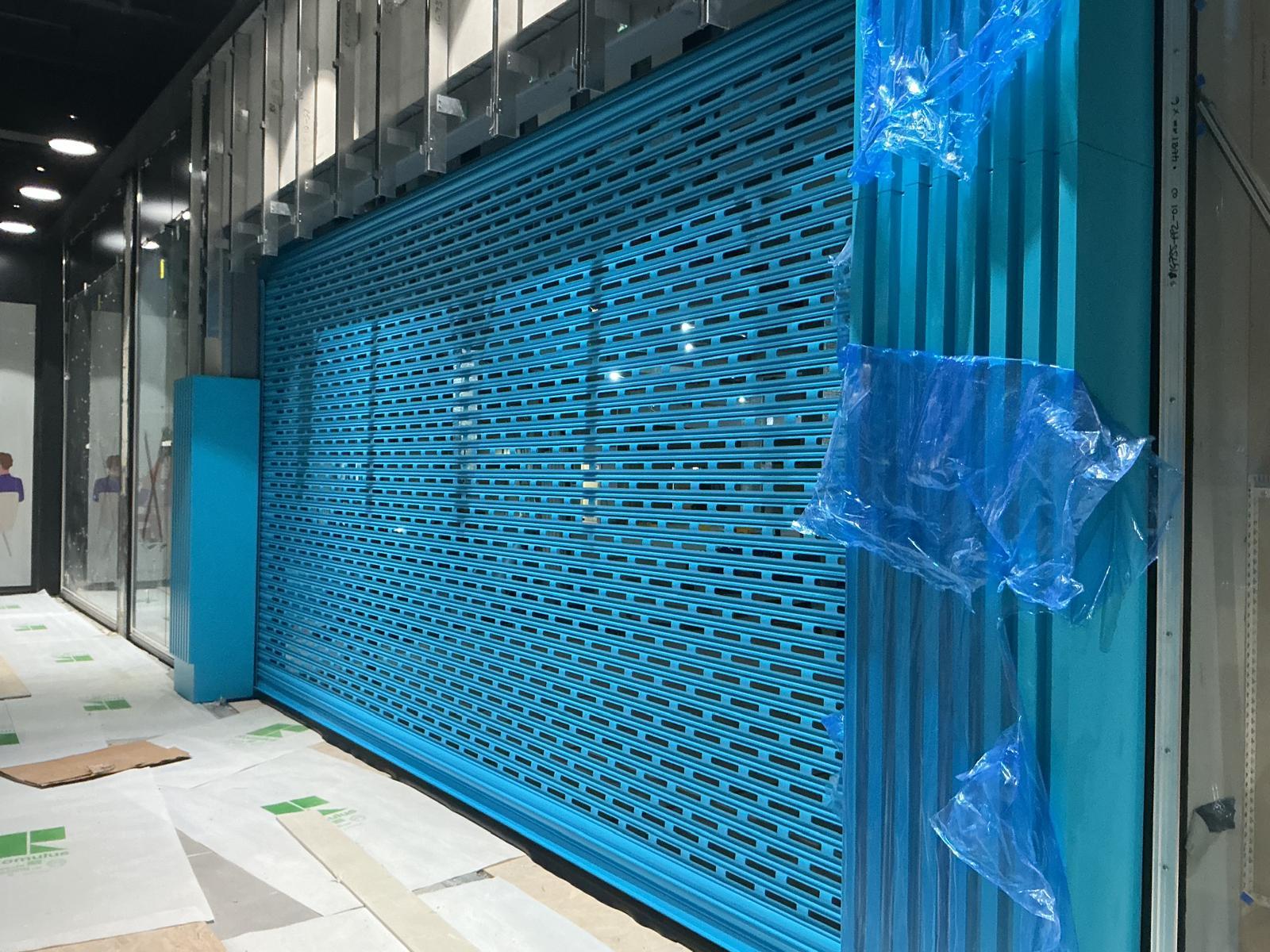 Blue punched-lath shutter installed to a retail opening