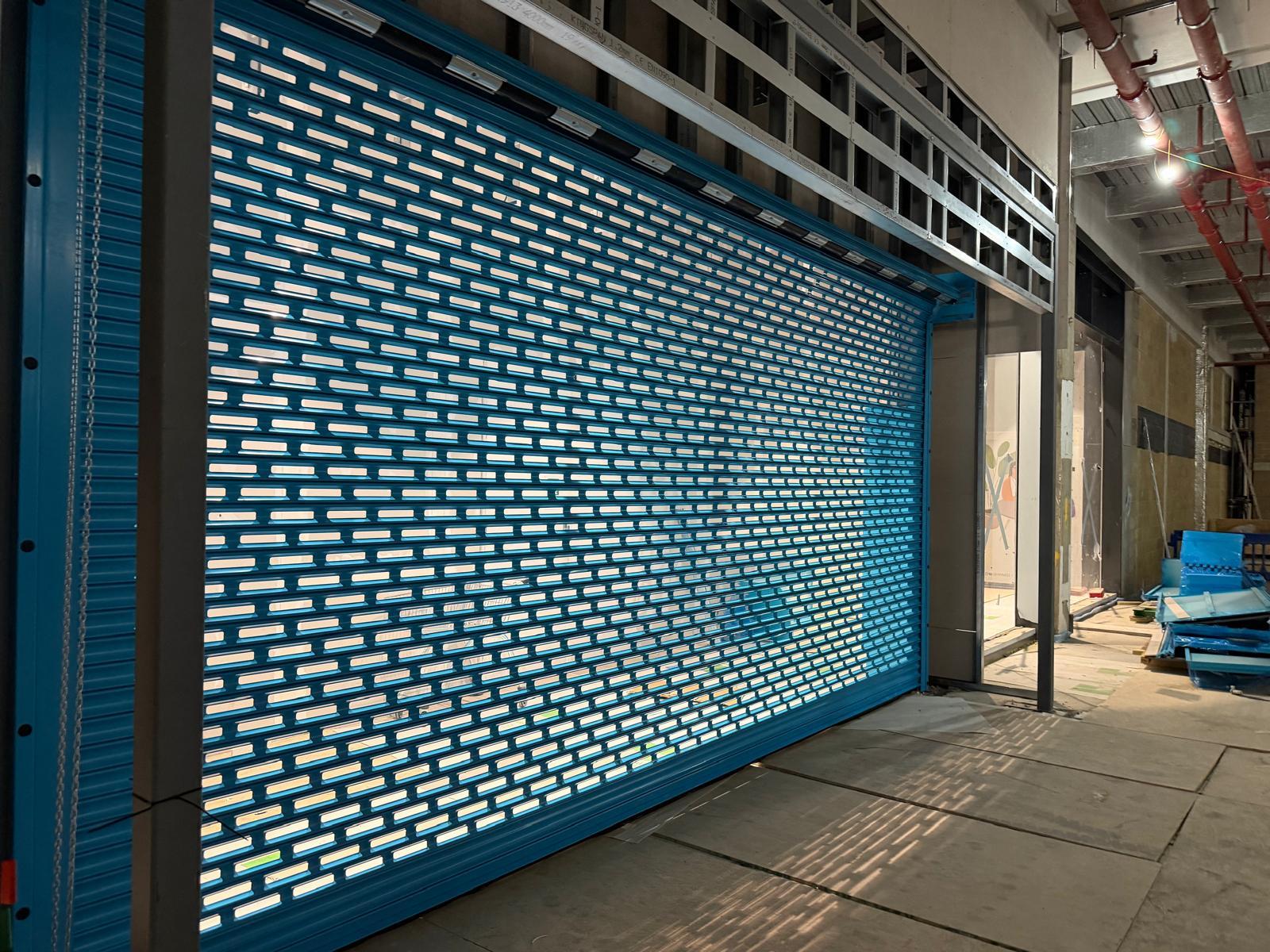 Punched-lath security shutter across a glazed retail frontage