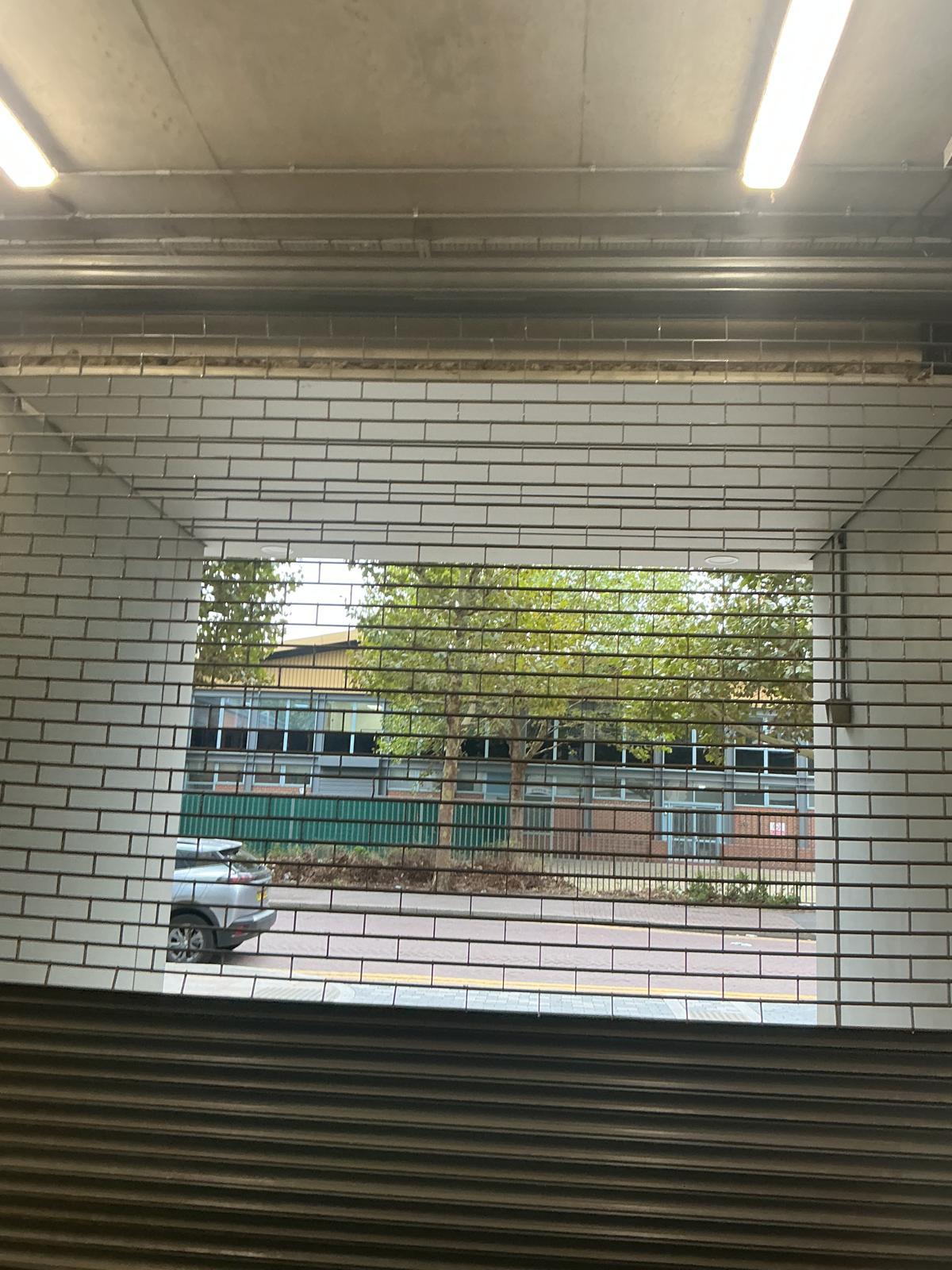 Punched-lath security shutter closed over a shopfront, the display still visible through the perforations