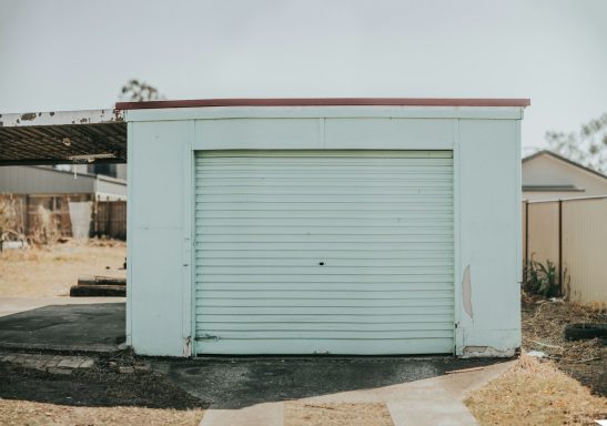 Light blue garage with a white roller door, set in a grassy area.